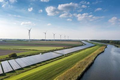 wind turbines and solar panels beside a river with blue skies and green fields